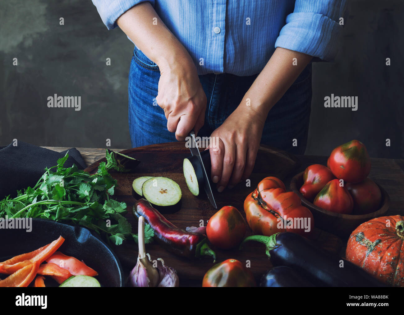 Weibliche Hände schneiden Aubergine auf Holzbrett für veganes Essen. Stockfoto