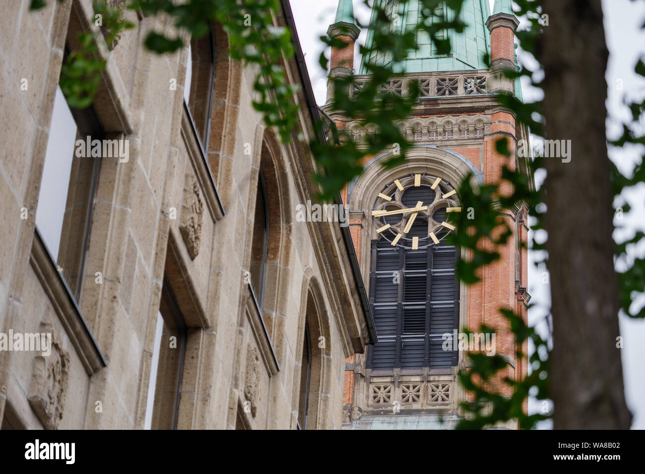 Low Angle View und ausgewählten Schwerpunkte durch die Blätter des Baums auf goldene Uhr Turm der Johanneskirche, Johannes Kirche, evangelische Stadtkirche. Stockfoto