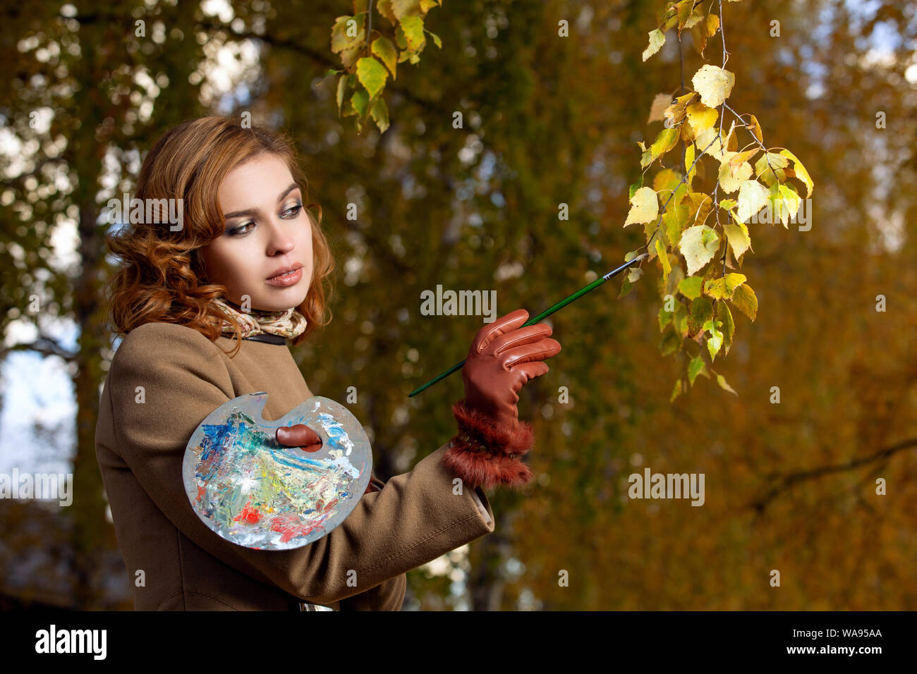 Junge schöne Frau mit Palette und Pinsel Lacke Farben Blätter an den Bäumen. Draußen im Herbst Park. Stockfoto