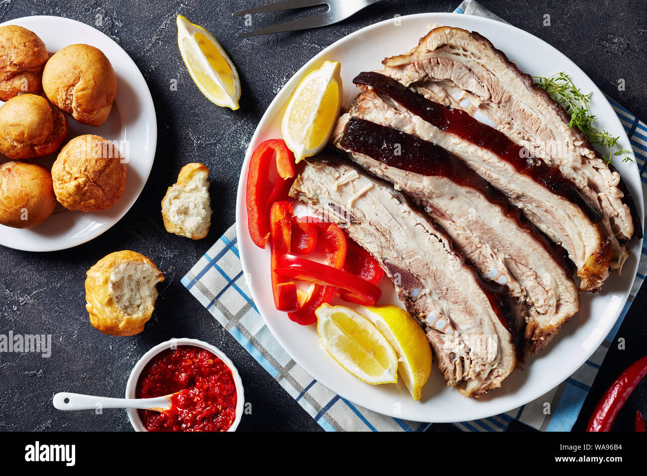Scheiben Schweinebraten Bauch auf eine weiße Platte mit jamaikanischen gebratene Knödel und Hot Pepper Sauce in einer Schüssel auf einer konkreten Tabelle, horizontale Ansicht von Abo Stockfoto