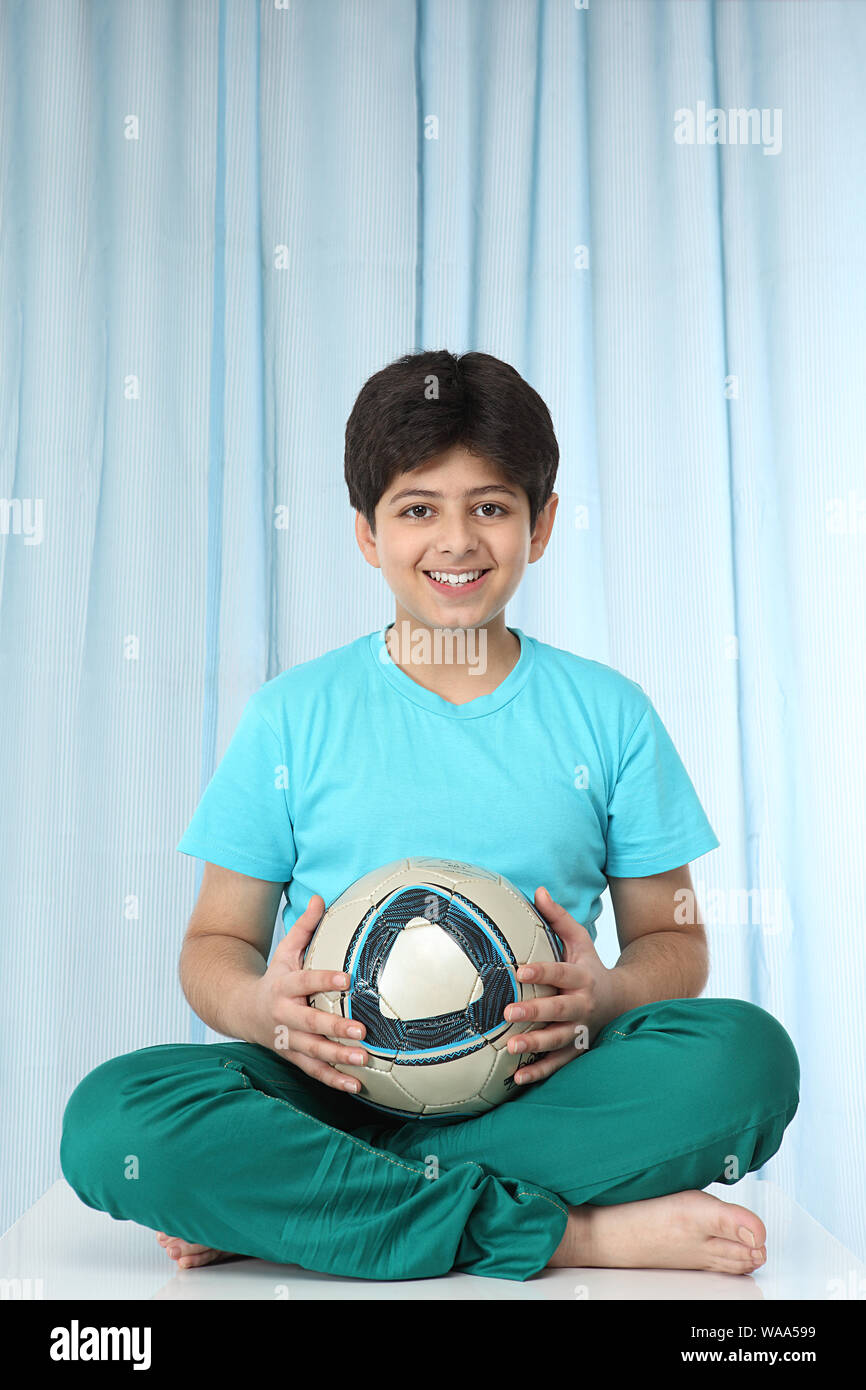 Junge sitzt mit Fußball und lächelt Stockfoto