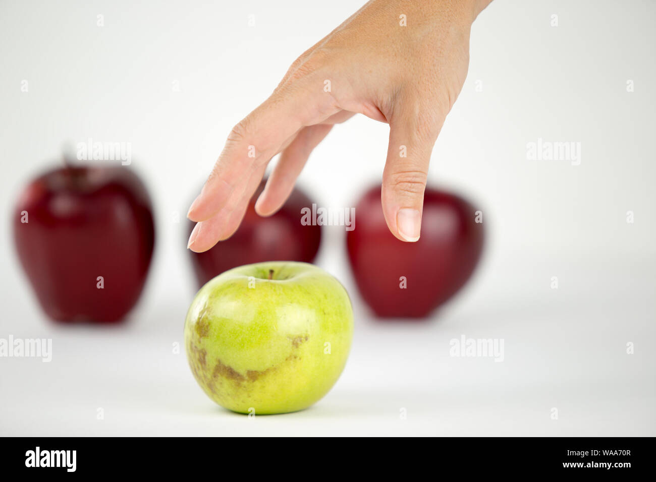 Konzept der Vielfalt: die Hand einer Frau ist über die einzige Green Apple unter den anderen roten zu ergreifen Stockfoto