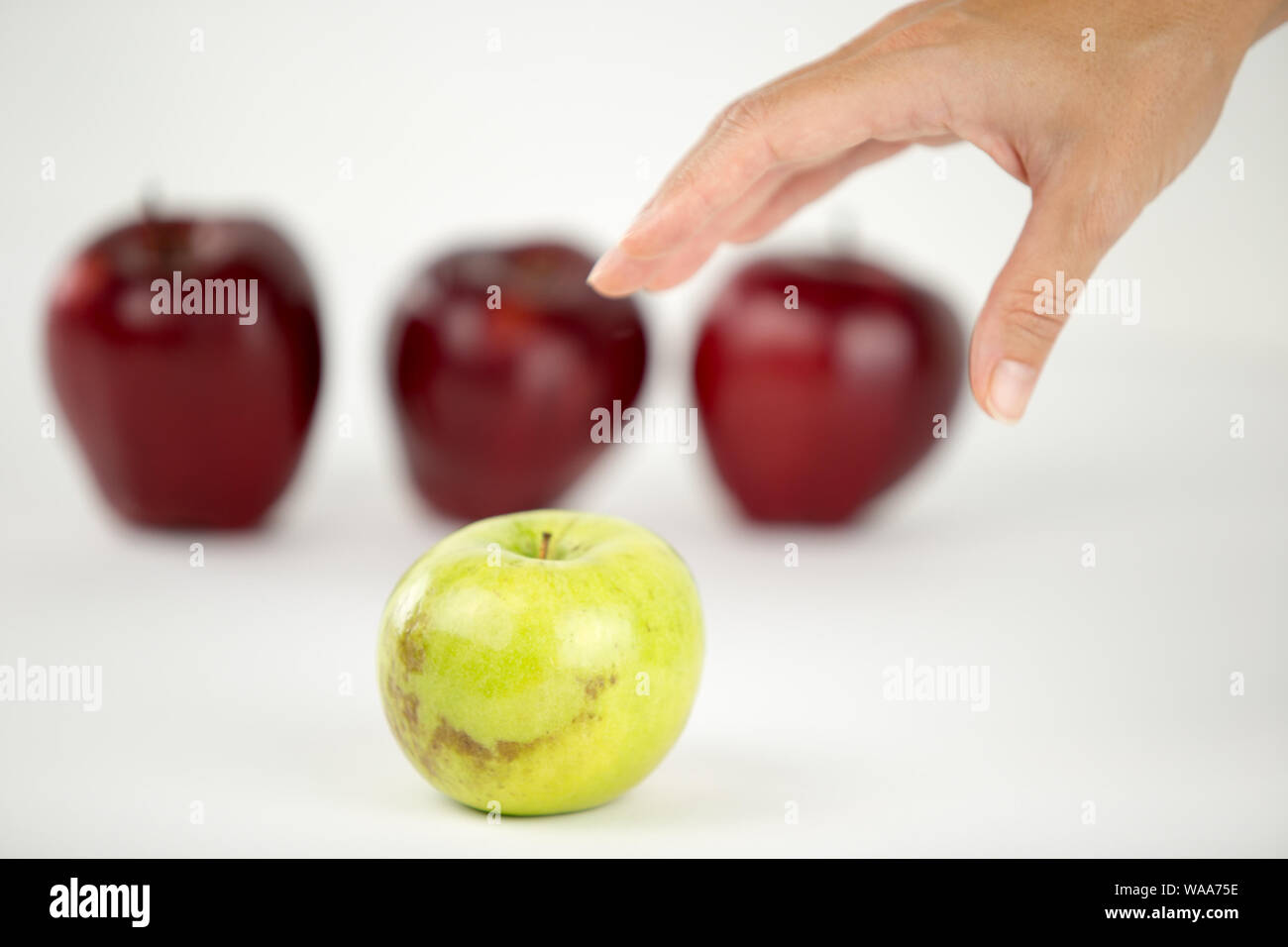 Konzept der Vielfalt: die Hand einer Frau ist über die einzige Green Apple unter den anderen roten zu ergreifen Stockfoto
