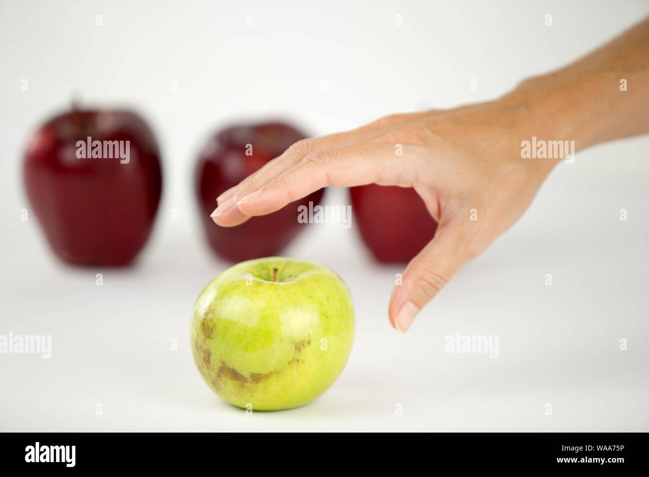 Konzept der Vielfalt: die Hand einer Frau ist über die einzige Green Apple unter den anderen roten zu ergreifen Stockfoto