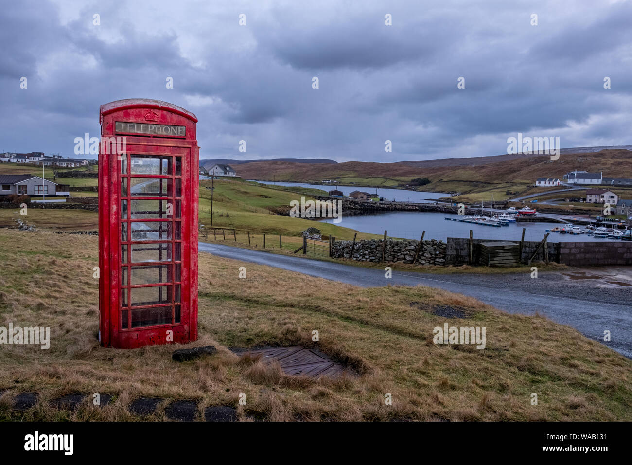 Eine helle rote Telefonzelle steht alleine in der Nähe einer Straße in ländlicher Lage in der Shetlandinseln, Schottland Stockfoto