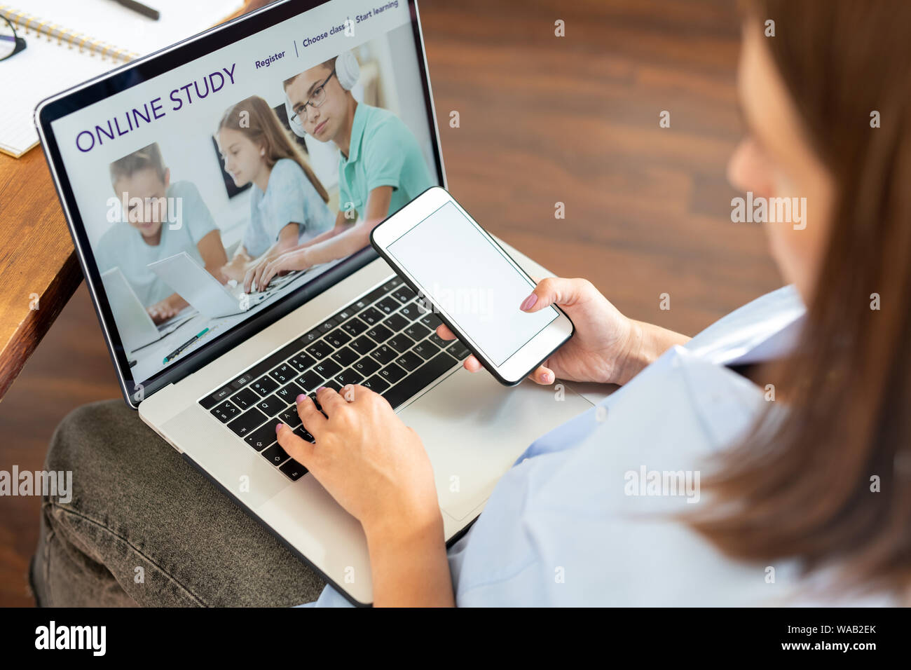 Junge Frau mit Smartphone sitzen vor dem Laptop Display Stockfoto