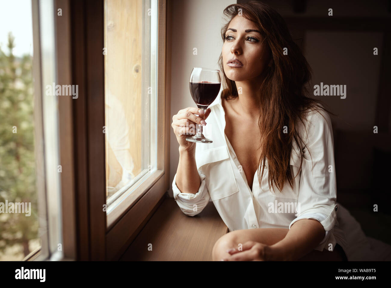 Junge traurige Frau trinkt Rotwein und schauen durch das Fenster, fühlt sich unglücklich und deprimiert, leiden unter Missbrauch, Belästigung oder Depressionen oder h Stockfoto