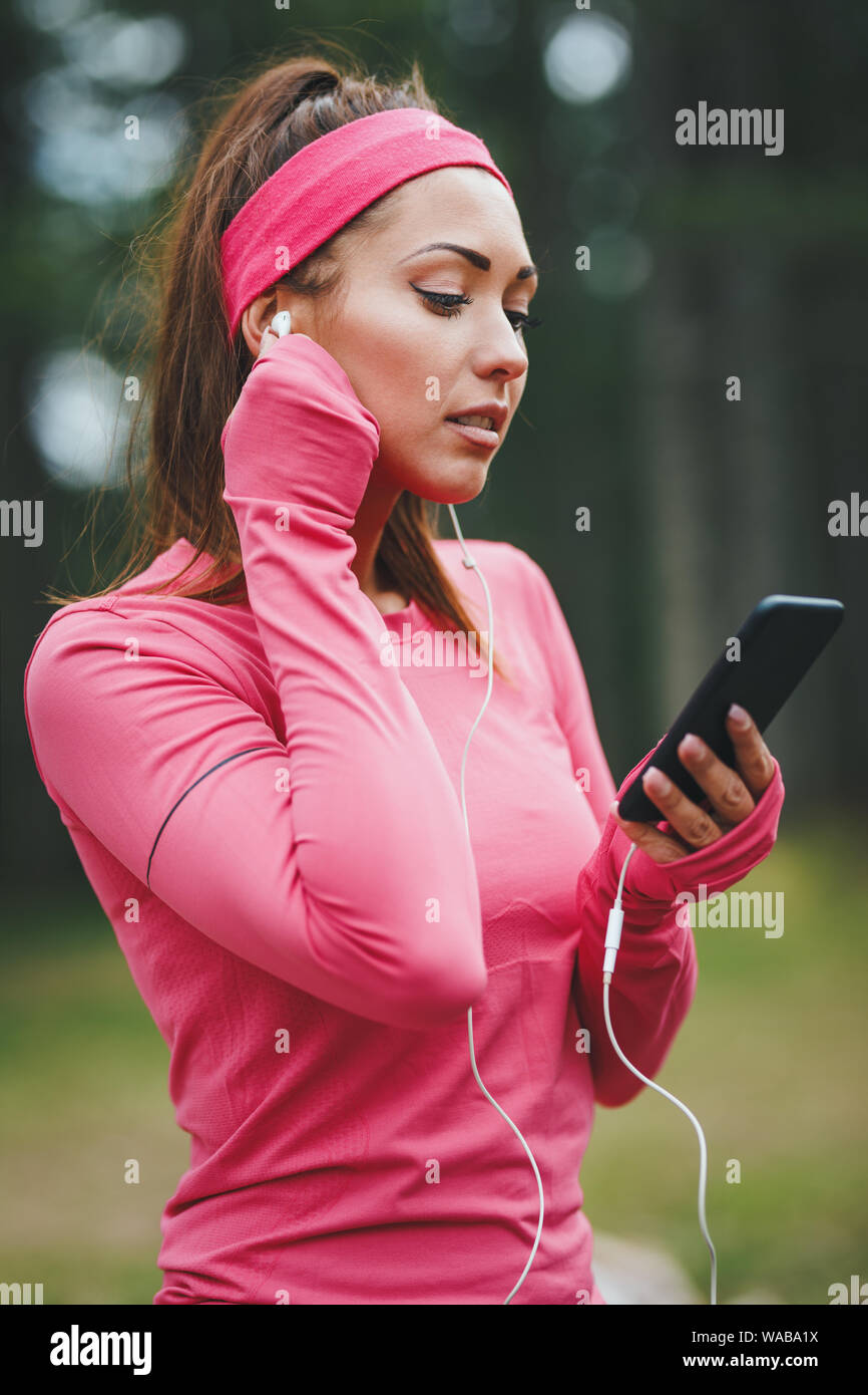 Junge Läuferin das Hören von Musik und eine Pause nach dem Joggen an einem sonnigen Wald. Stockfoto