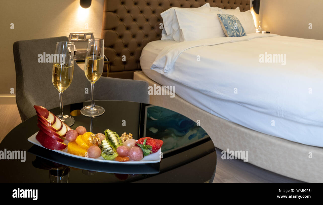2 Champagner Gläser mit einer Obstschale auf der Tischplatte mit Bett im Hintergrund Stockfoto