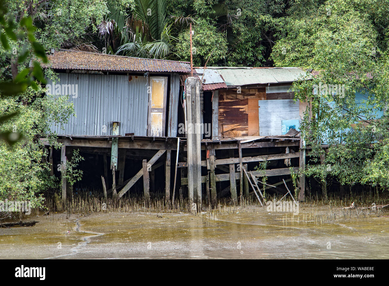 Schlechte Häuser auf den schlammigen Fluss. Metall Hütten stehen auf Holzbalken durch das Wasser. Stockfoto