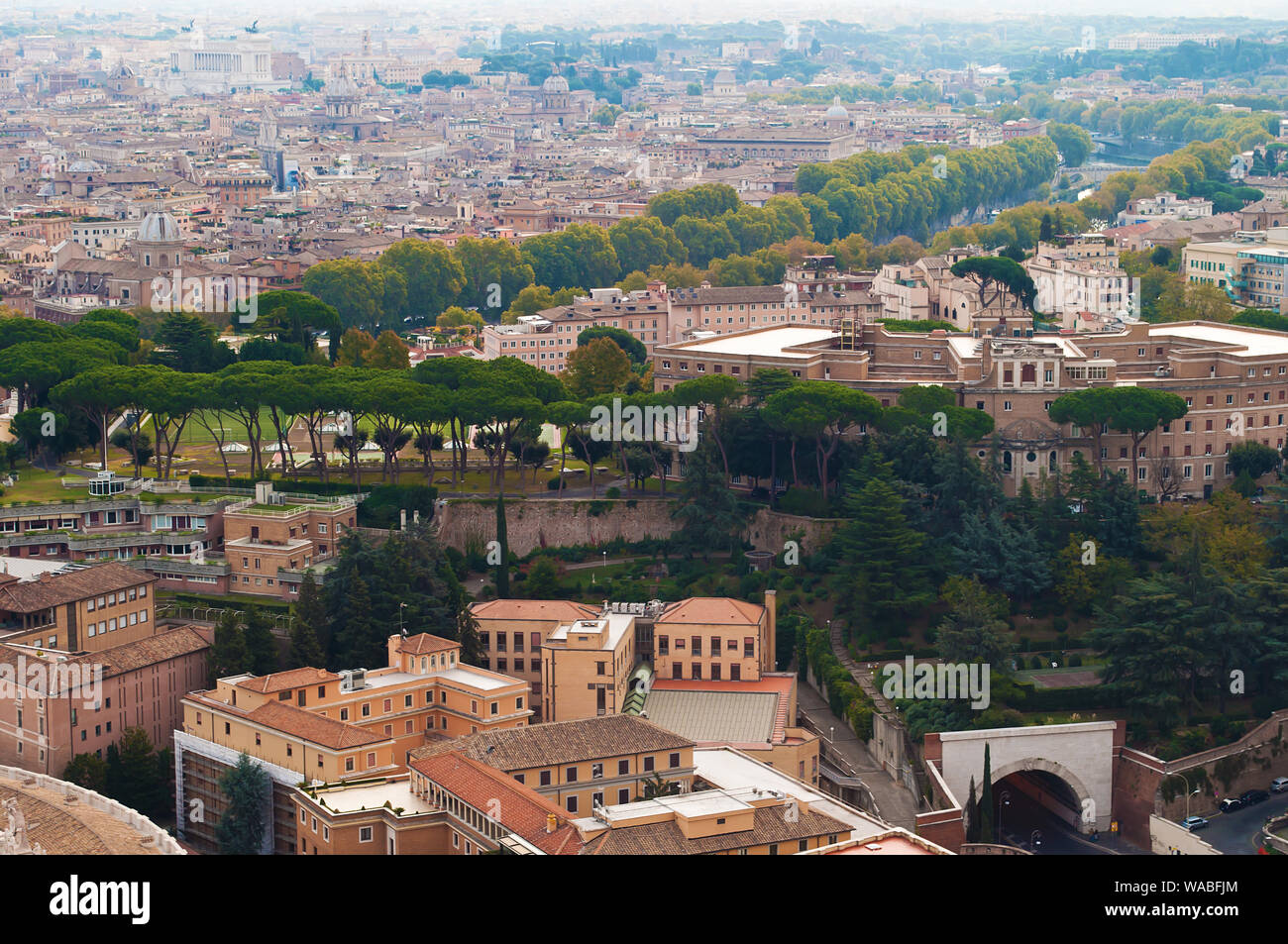 Blick auf viele orange Dächer und Reihen von hohen grünen Bäumen und Umrisse einer rauchigen Skyline, Rom, Italien. Sonnigen Herbsttag. Von oben geschossen Stockfoto