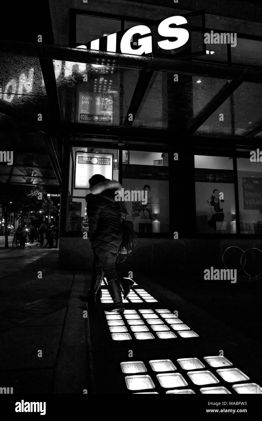 Street Fotografie Druck eines Vancouver Downtown Nacht Szene. Ein Stadtbild städtische Foto der Lichter auf die Straße und eine Frau, die durch Sie. Stockfoto