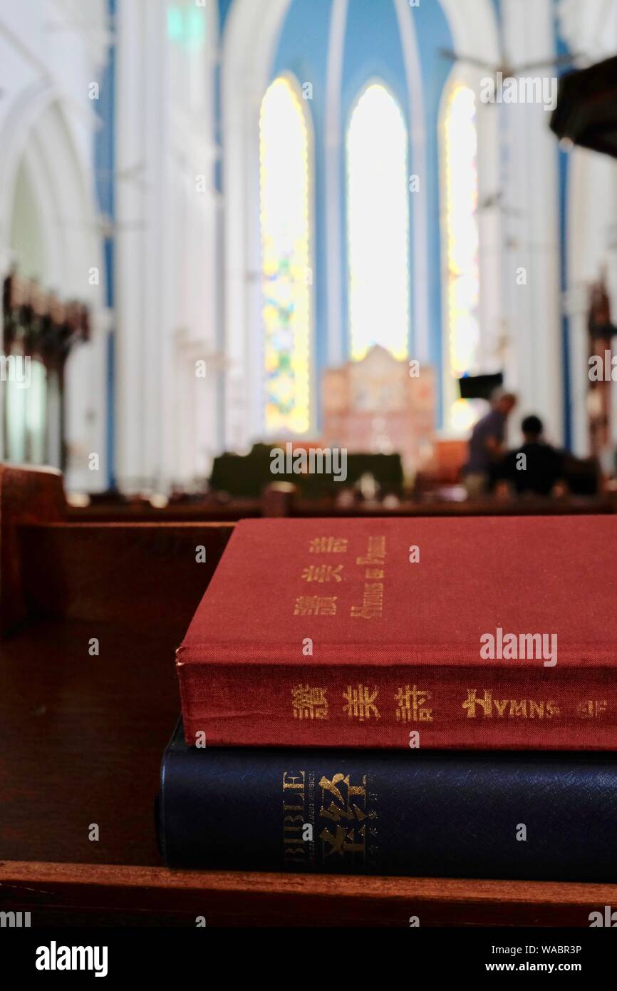 Singapur: Bibel und Gebet Buch auf Chinesisch auf der Kirchenbank bei St. Andrew's Cathedral, die Kirche innen und Windows im Hintergrund Stockfoto