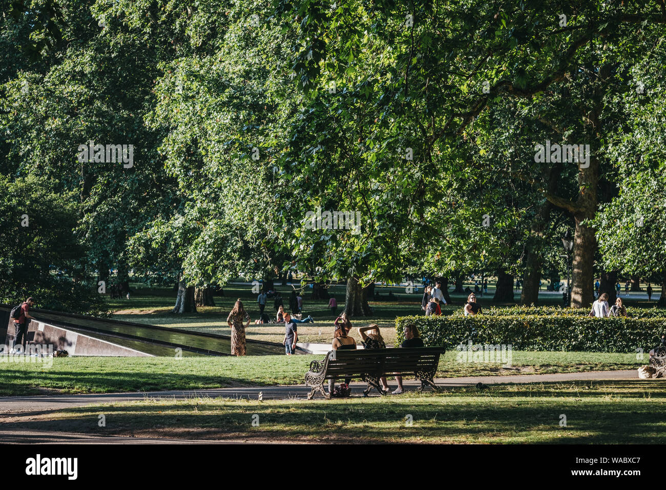 London, Großbritannien - 15 Juli, 2019: die Menschen entspannen auf einer Bank in einem Park an einem heissen Sommertag in London, UK. London erlebt eine Reihe von Hitzewellen in 2019. Stockfoto