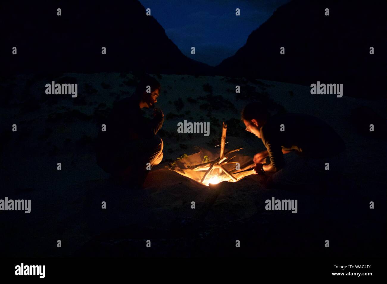 Kontemplative Jungs machen ein Feuer am Strand & Berge hinter Ihnen. Stockfoto