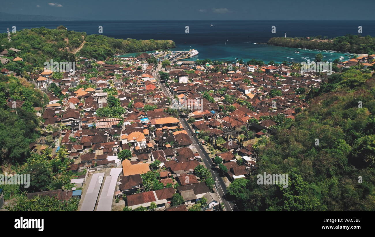 Luftbild Drohne Flug über den grünen Berg, Red Roof Dorf und Meer Hafen mit Fähren Pier. Erstaunliche Natur Landschaft. Tropische Insel Bali, Indonesien Stockfoto