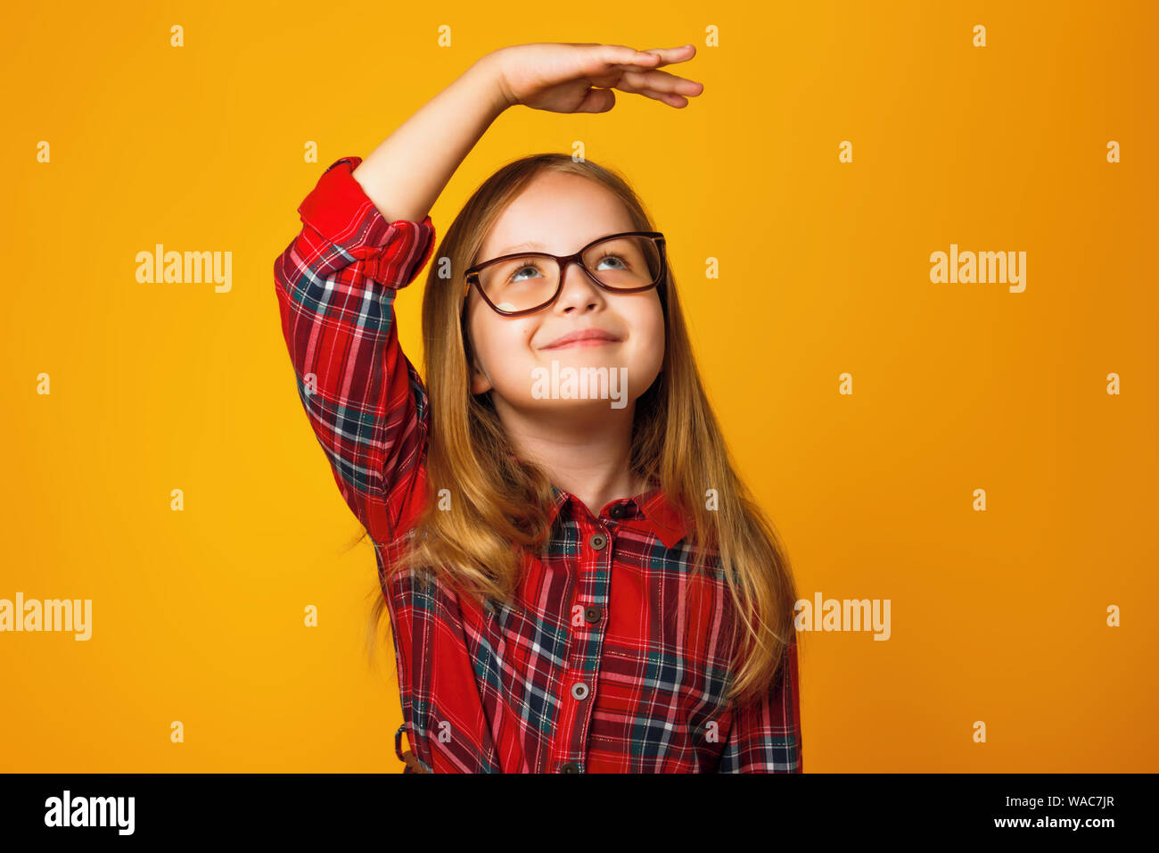 Closeup Portrait eines kleinen Mädchens auf einem gelben Hintergrund. Ein Kind mit einer Brille Maßnahmen seine Höhe. Stockfoto