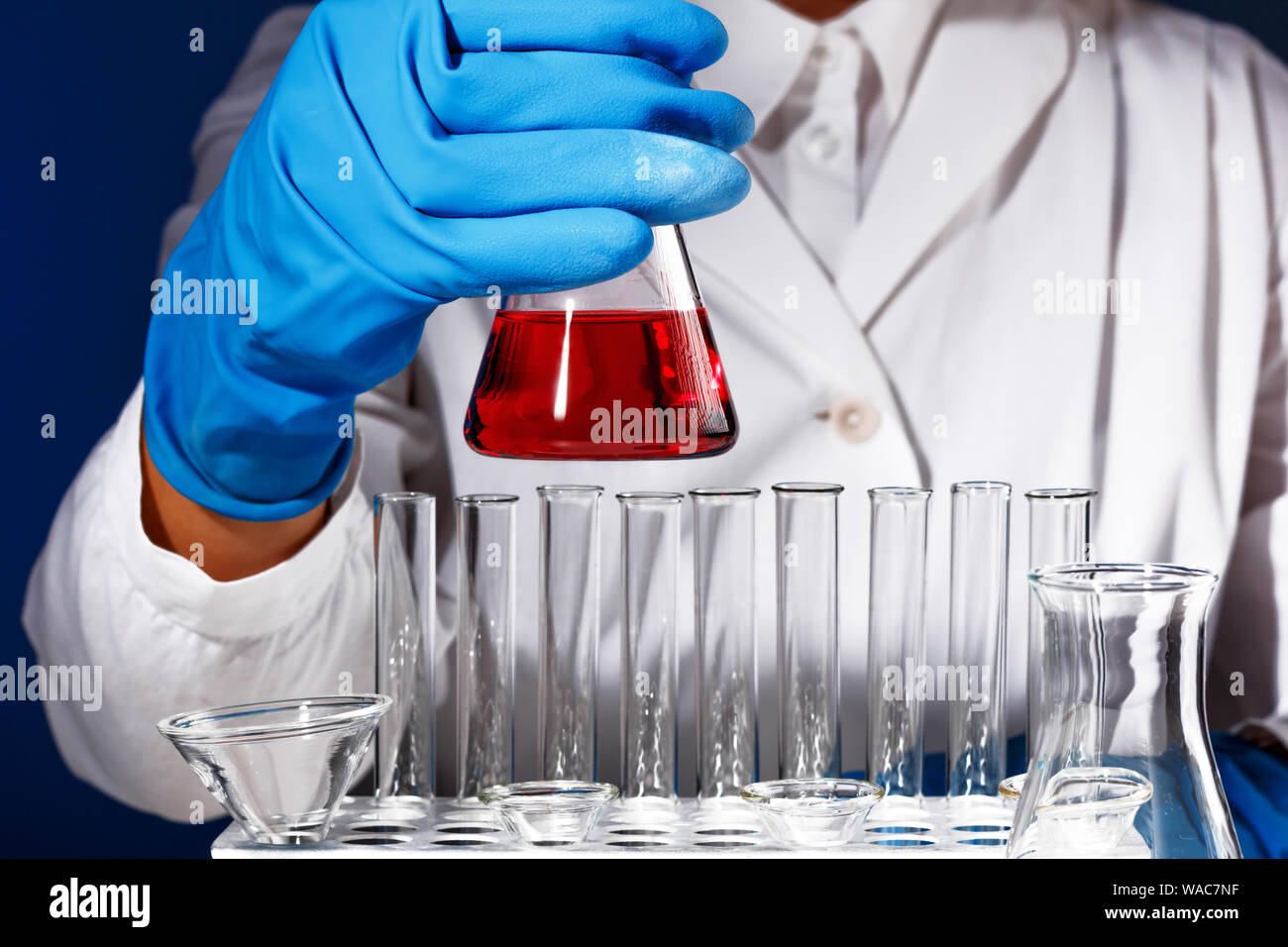 In einem Chemielabor, ein Mann ist Apotheker eine Flasche mit roter Flüssigkeit analysieren. Medizinischen Experiment mit einem Rohr. Chemiker arbeitet auf einem Test mit blau Handschuh Stockfoto