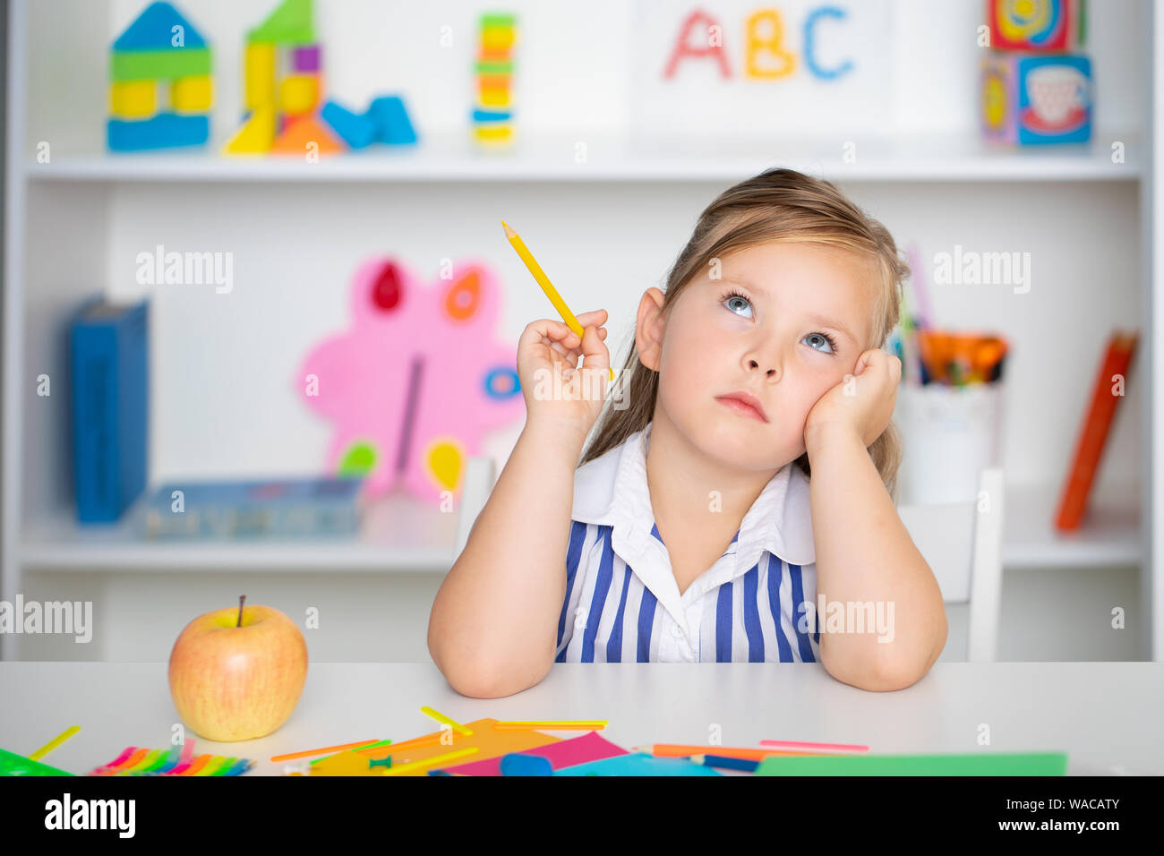 Süße kleine Mädchen träumt am Tisch hält einen Bleistift in der Hand Stockfoto