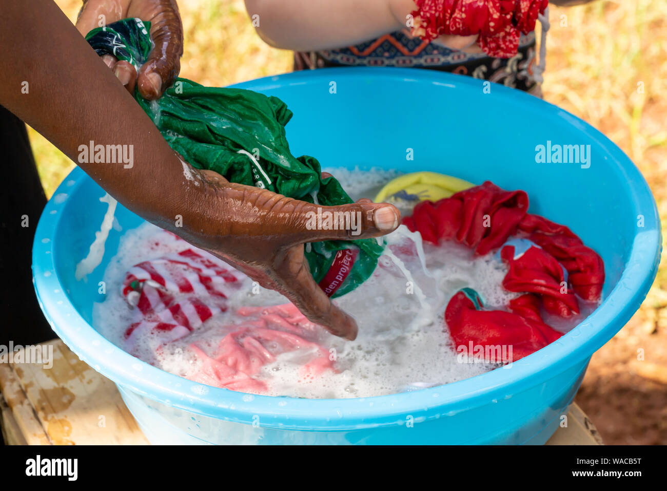 Nanyuki, Kenia - 13. Juni 2019: Farbfoto des kenianischen Frau hand Wäsche waschen in blauer Schüssel mit nur Hände sichtbar. Stockfoto