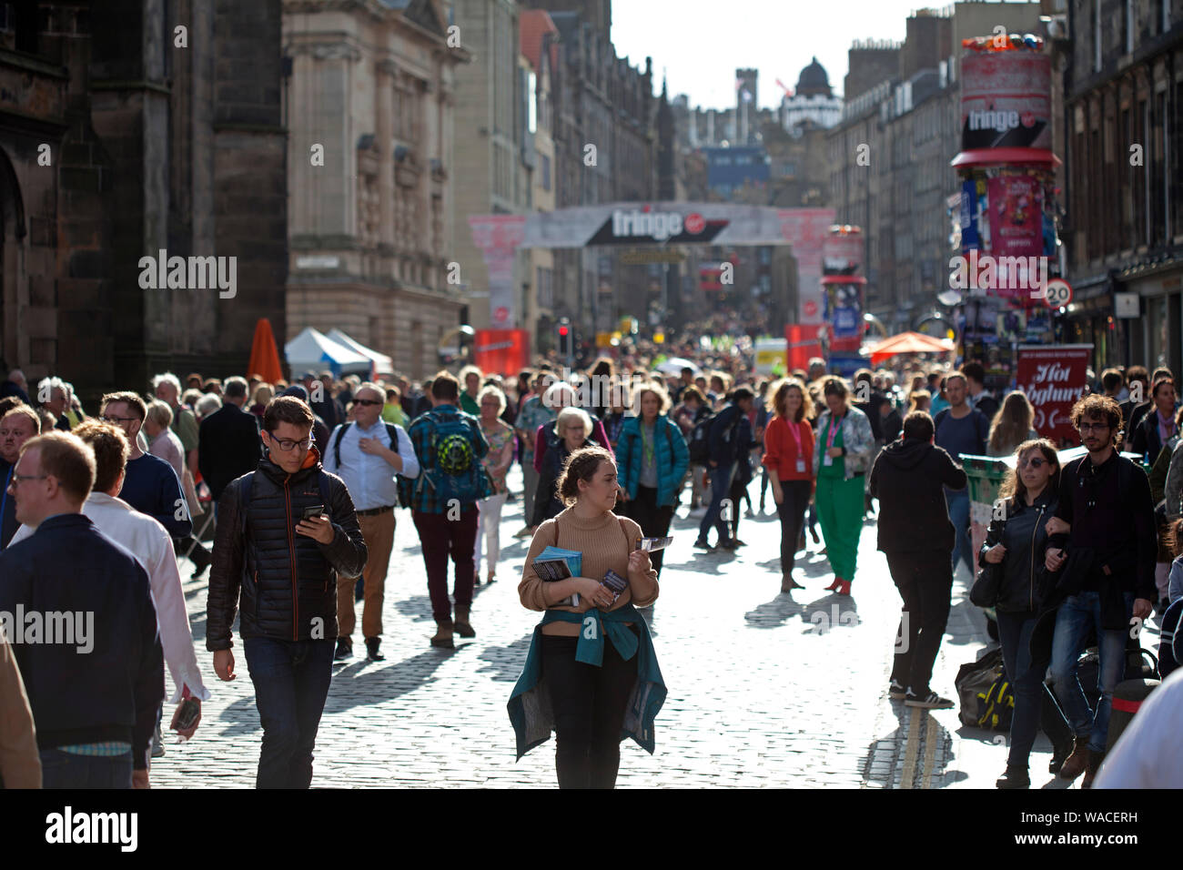 Edinburgh Fringe, Royal Mile, Schottland, Großbritannien. August 2019. Sonniger Abend nach einem sehr wechselhaften Tag für Darsteller auf der High Street. Menschenmassen gehen in der Sonne hinunter. Stockfoto