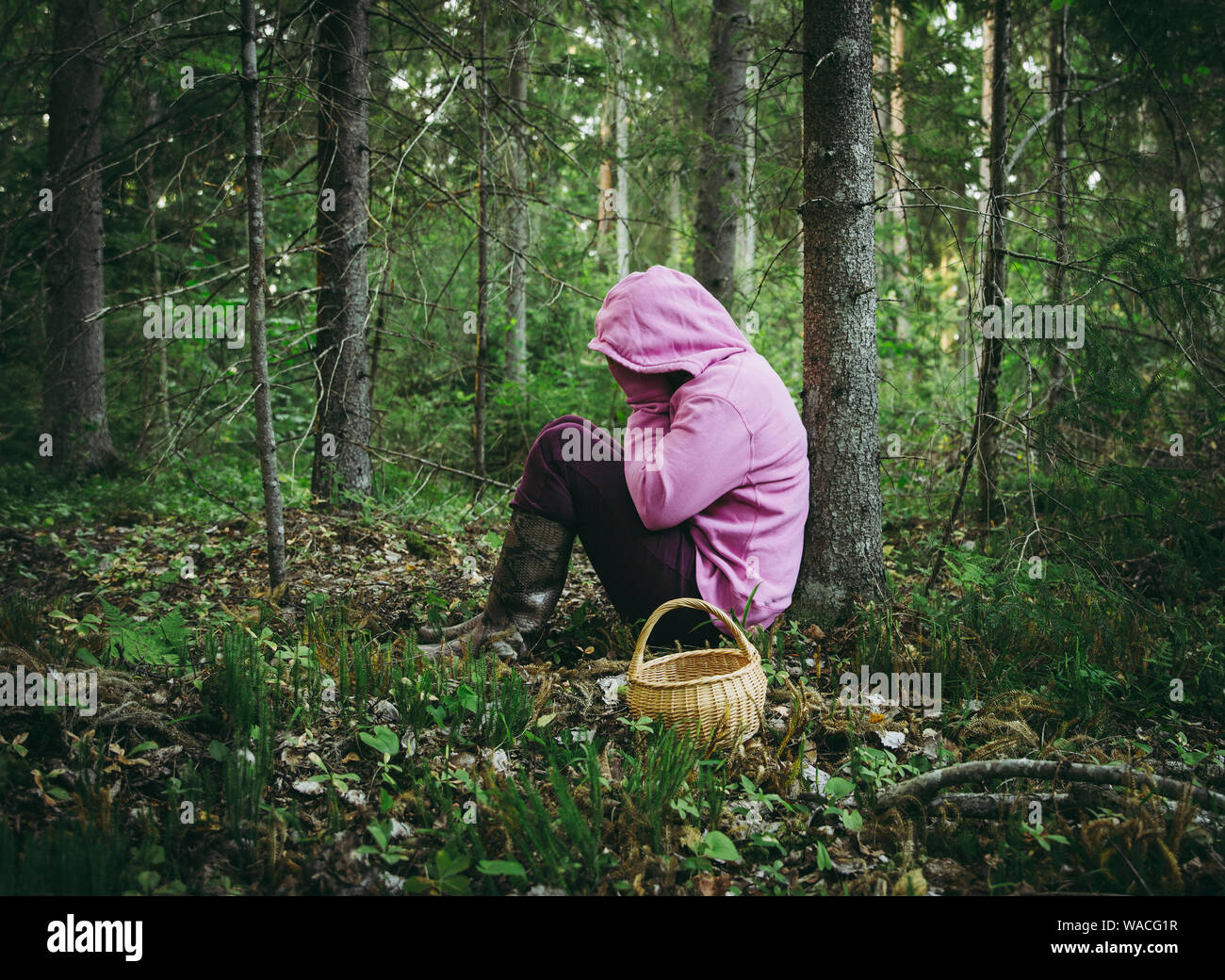 Verwirrt Person ging zum Pilze sammeln und haben sich im Wald verirrt, verwirrt, verängstigt und verwirrt, Nordeuropa, unter dem Baum sitzen. Person verloren in Stockfoto