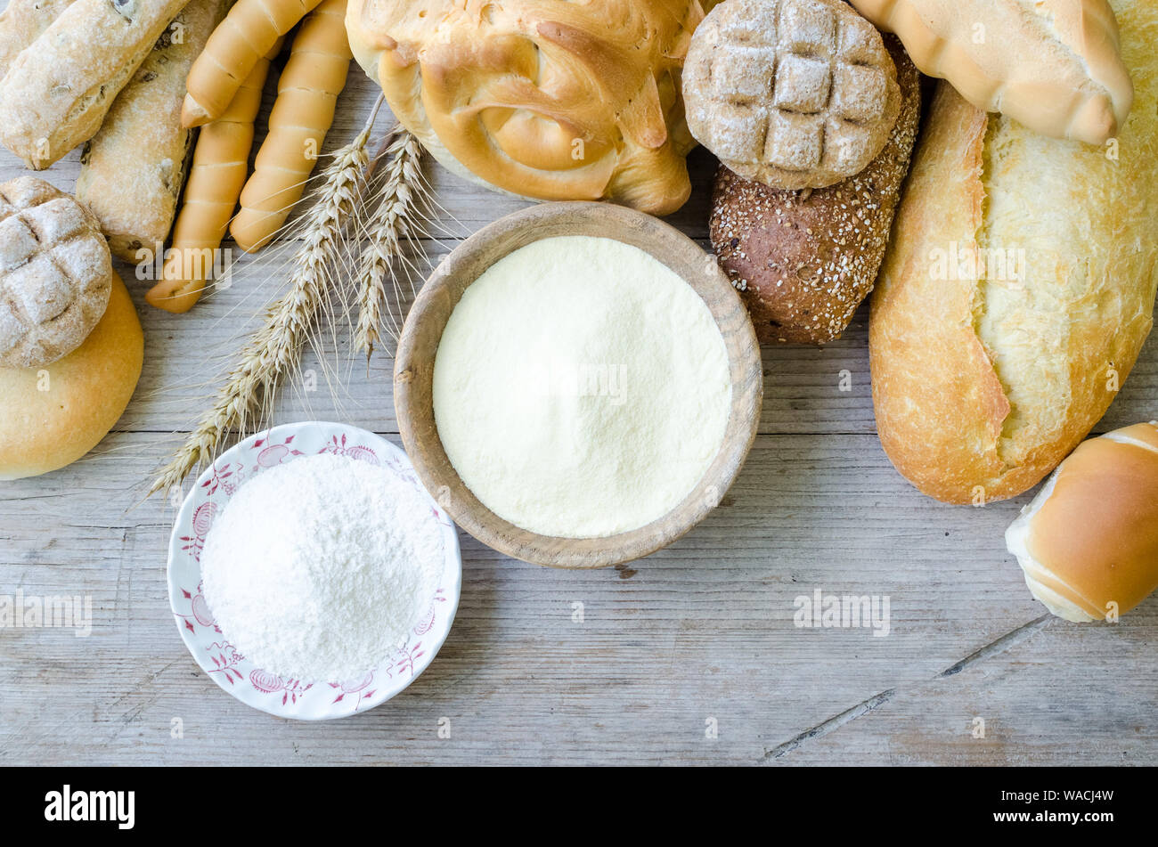 Verschiedene Arten von traditionellen Italienischen frisch gebackenes Brot und Brötchen mit Schüssel Mehl auf hölzernen Tisch Hintergrund. Rustikale Vintage Style. Ansicht von oben. Stockfoto