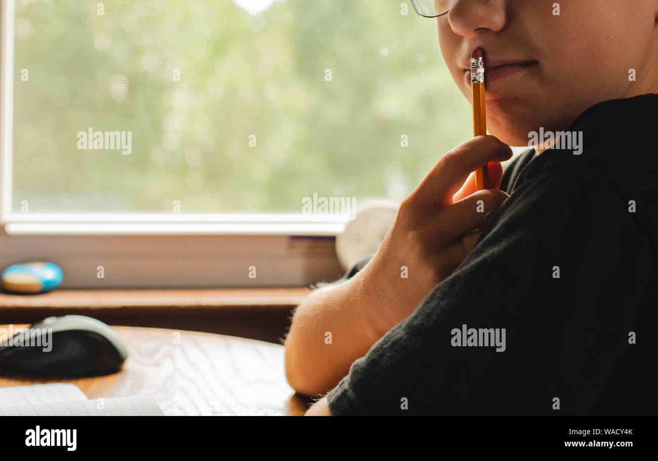 Ein Junge mit der Spitze eines Stifts, der auf seinen Mund, während er denkt über etwas. Stockfoto