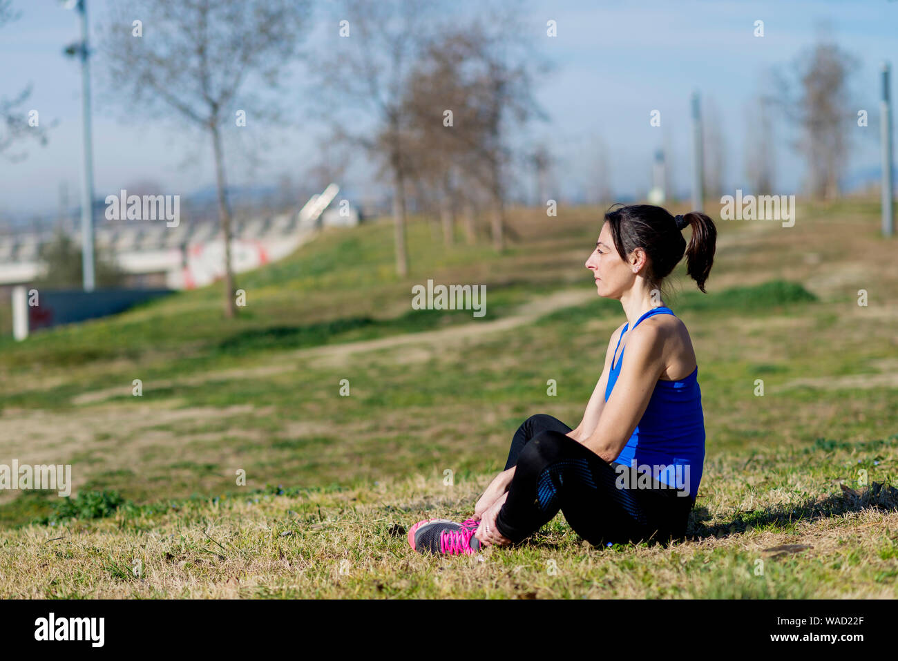Weibliche Athleten meditieren beim Sitzen auf dem Rasen im Park im sonnigen Tag Stockfoto