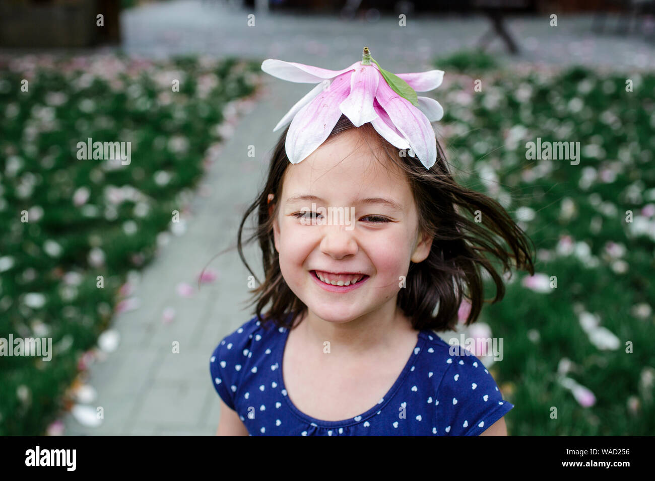 Eine lachende Mädchen mit Verwehten Haare trägt eine Blume für einen Hut Stockfoto