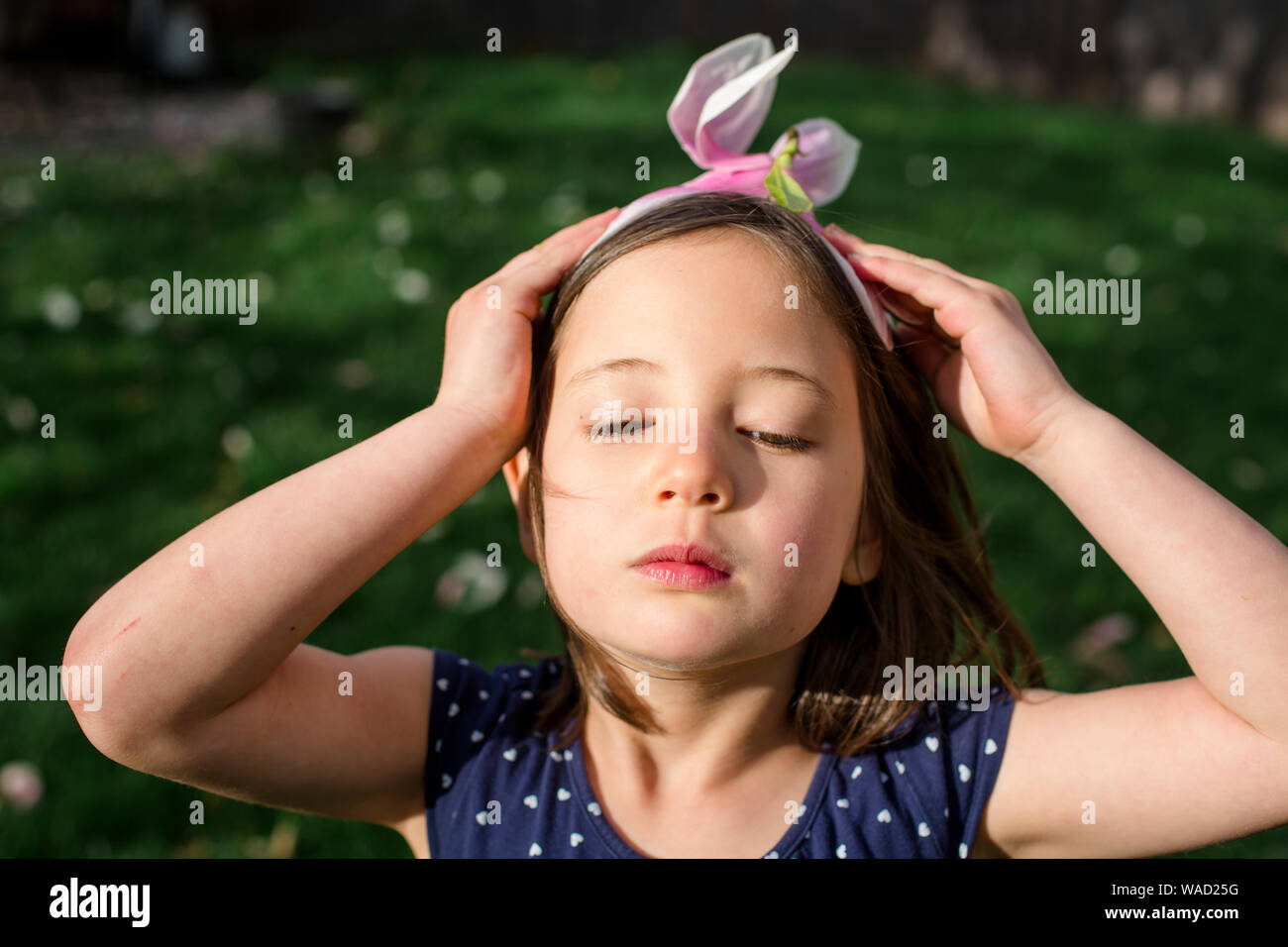 Ein wunderschönes kleines Mädchen mit ernsten Ausdruck trägt Blume für einen Hut Stockfoto
