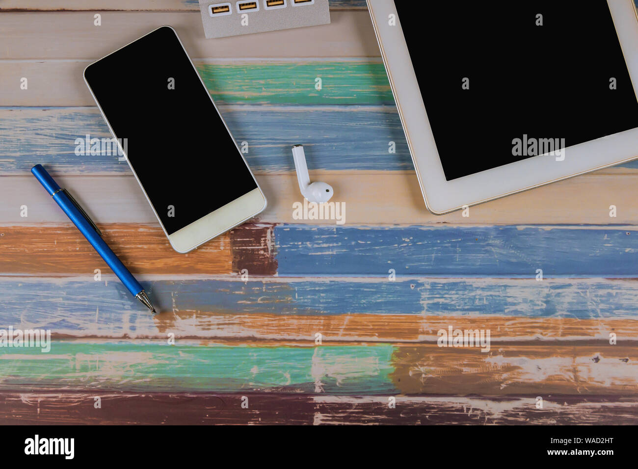 Tablet, Telefon, drahtlose Kopfhörer und Stift auf dem bunten Tisch. Stockfoto