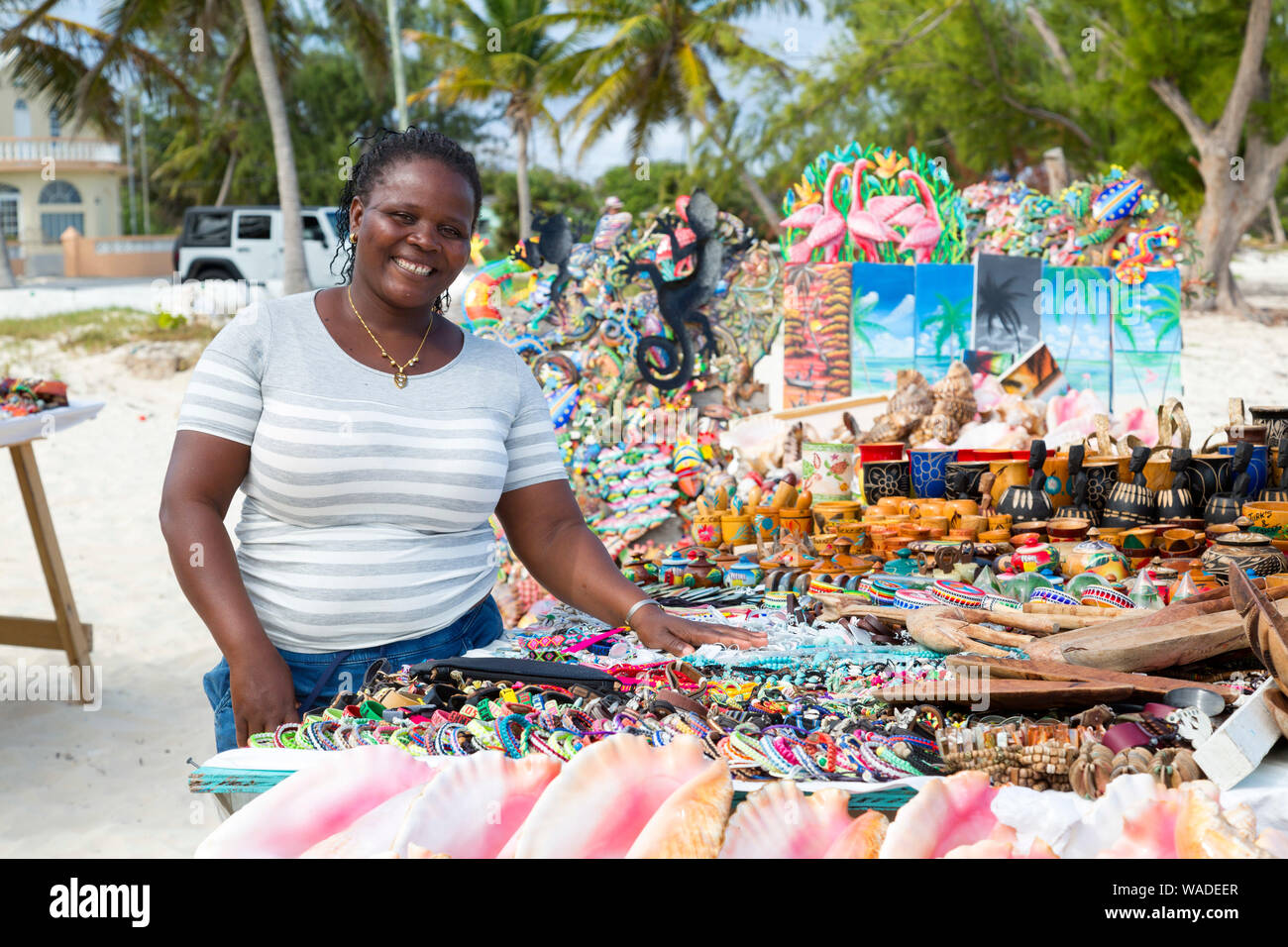 Lächelnde junge Dame zeigt Ihre Anzeige von Souvenirs am Strand in Turks- und Caicosinseln. Stockfoto