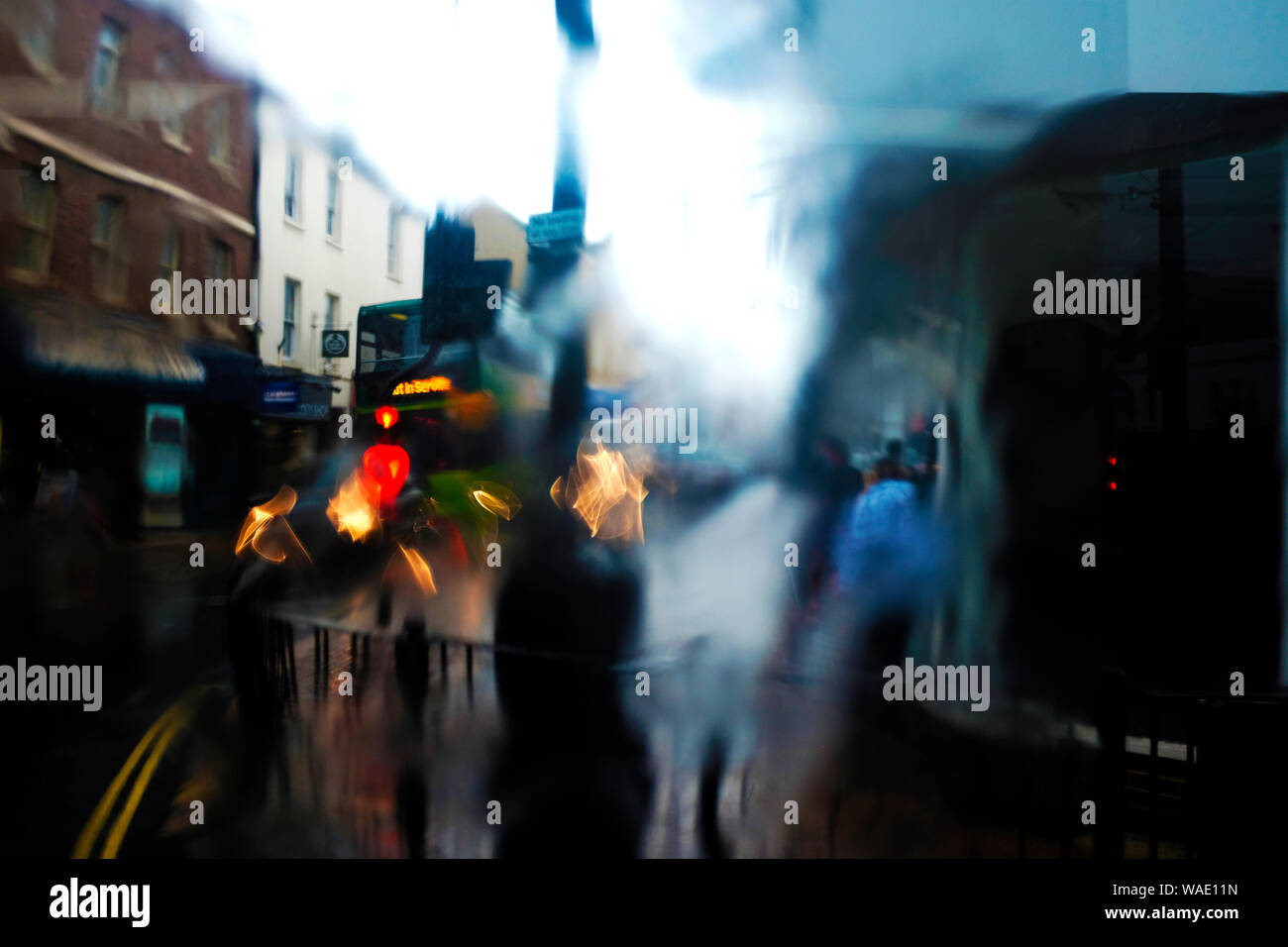 Blick auf der Beifahrerseite blurry Fußgänger aus Bus-Fenster auf nassen regnerischen Tag mit Wasser nach unten läuft der Bus Fensterbereich. Stockfoto
