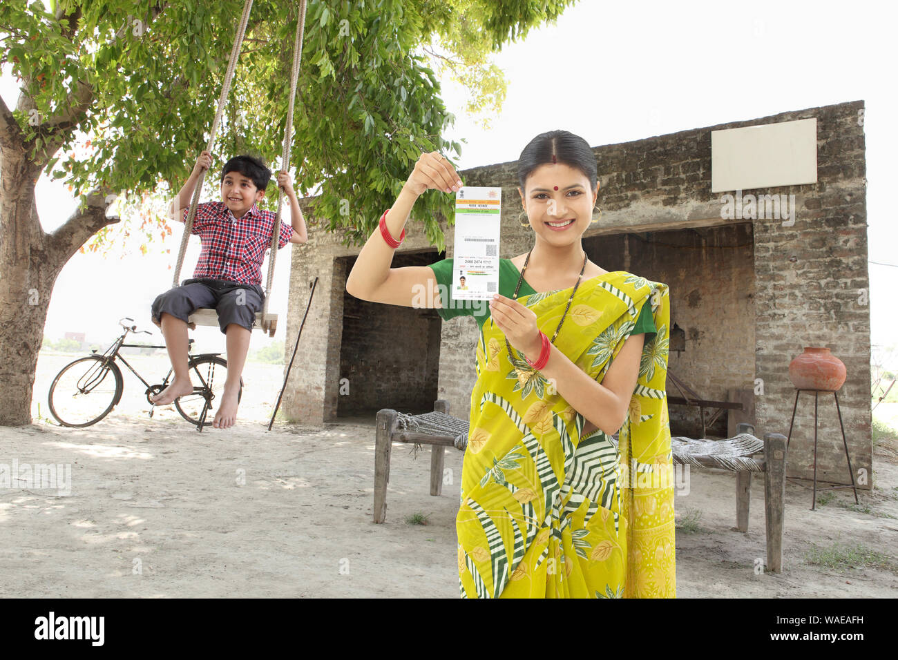 Eine ländliche Frau zeigt eine Aadhar-Karte mit ihrem Sohn, der schwingt Stockfoto