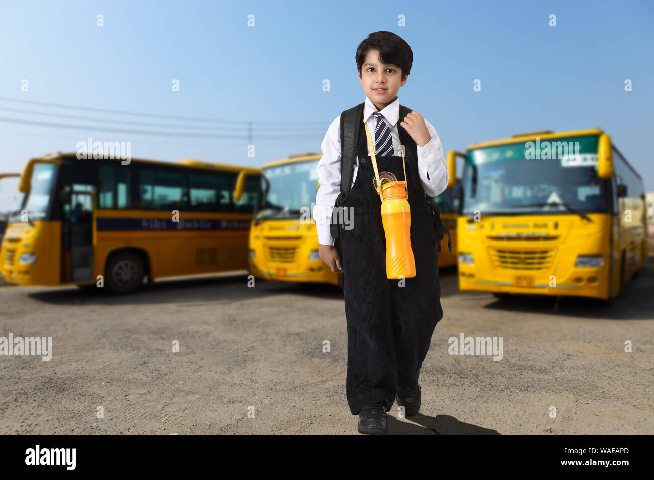 Schuljunge steht mit Schulbussen im Hintergrund Stockfoto