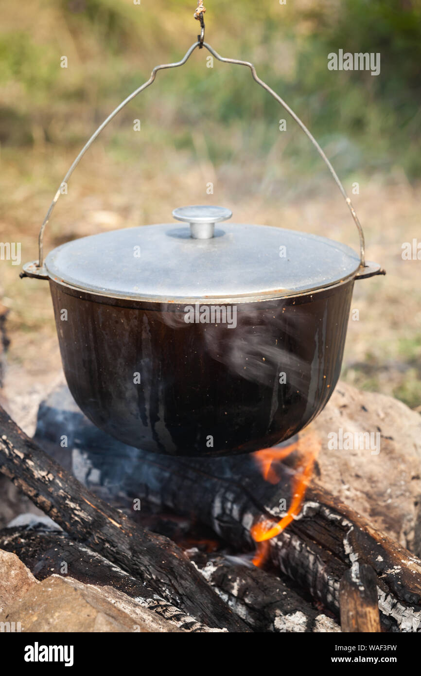 Lagerfeuer und schwarze Kessel. Vorbereitung einer Suppe auf offenem Feuer, Camping Mahlzeit. Vertikale Foto Stockfoto