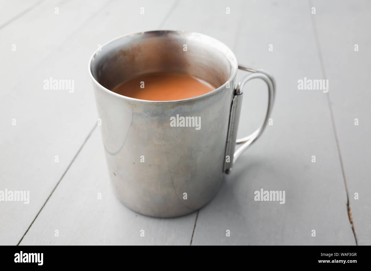 Metall Becher Kaffee mit Milch steht auf einem weißen Holztisch, closeup Foto mit selektiven Fokus Stockfoto