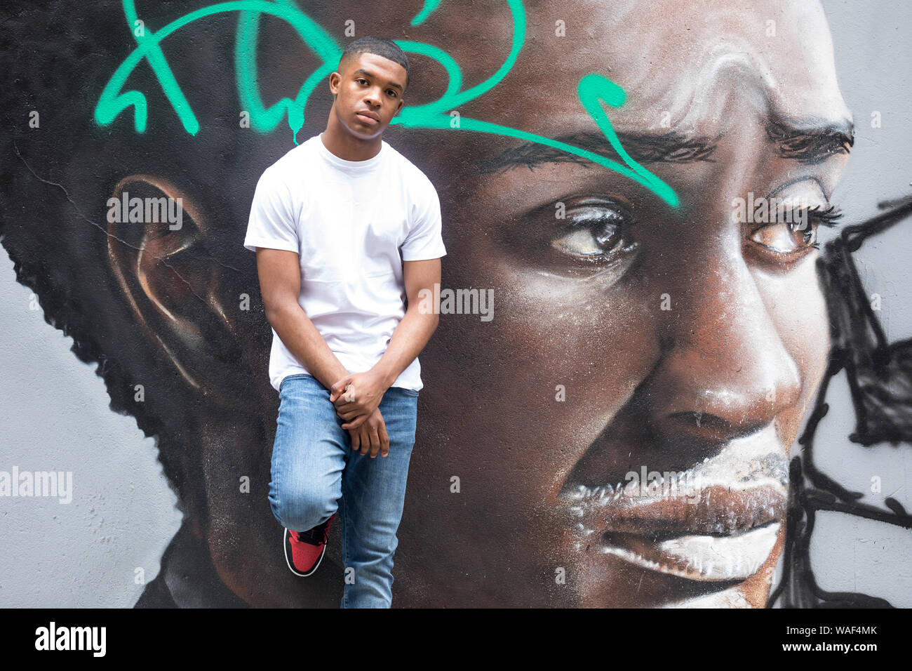 Ein junger Mann stellt sich vor einer grafitti Mauer Portrait einer Stadt Street in London. Stockfoto