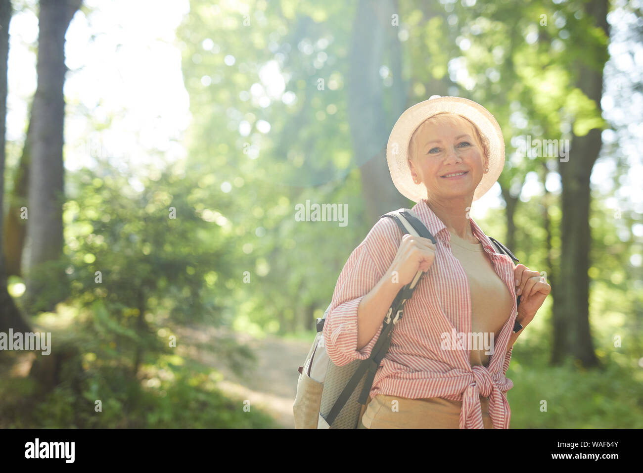 Portrait von reife Frau in lässige Kleidung und mit Rucksack lächelnd an Kamera und genießen den Spaziergang im Freien Stockfoto