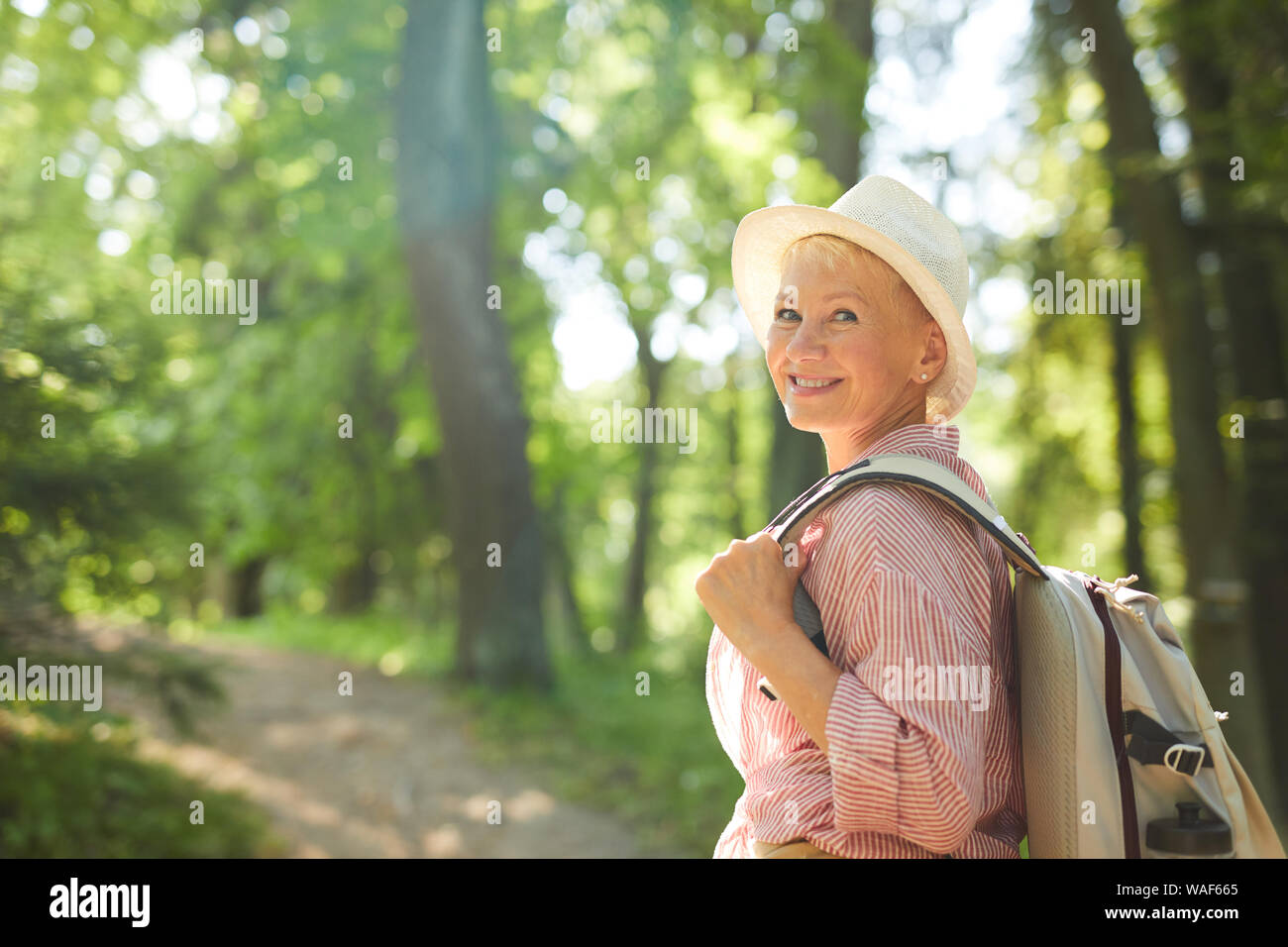 Portrait von reife Frau in Freizeitkleidung mit Rucksack lächelnd in die Kamera während ihrer Reise im Freien in den Wald Stockfoto