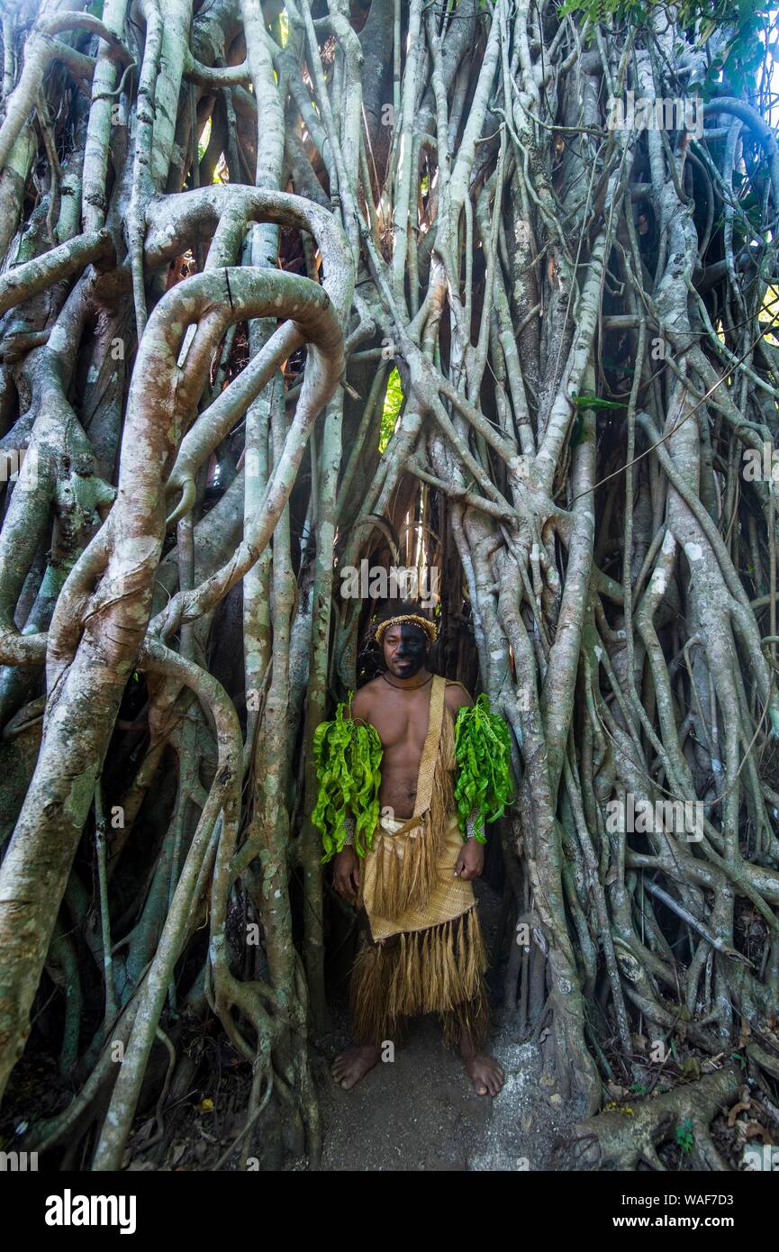 Traditionelle gekleideter Mann mit schwarzen Gesicht stehen in einem riesigen Banyon Tree, Ekasup Cultural Village, Efate, Vanuatu Stockfoto