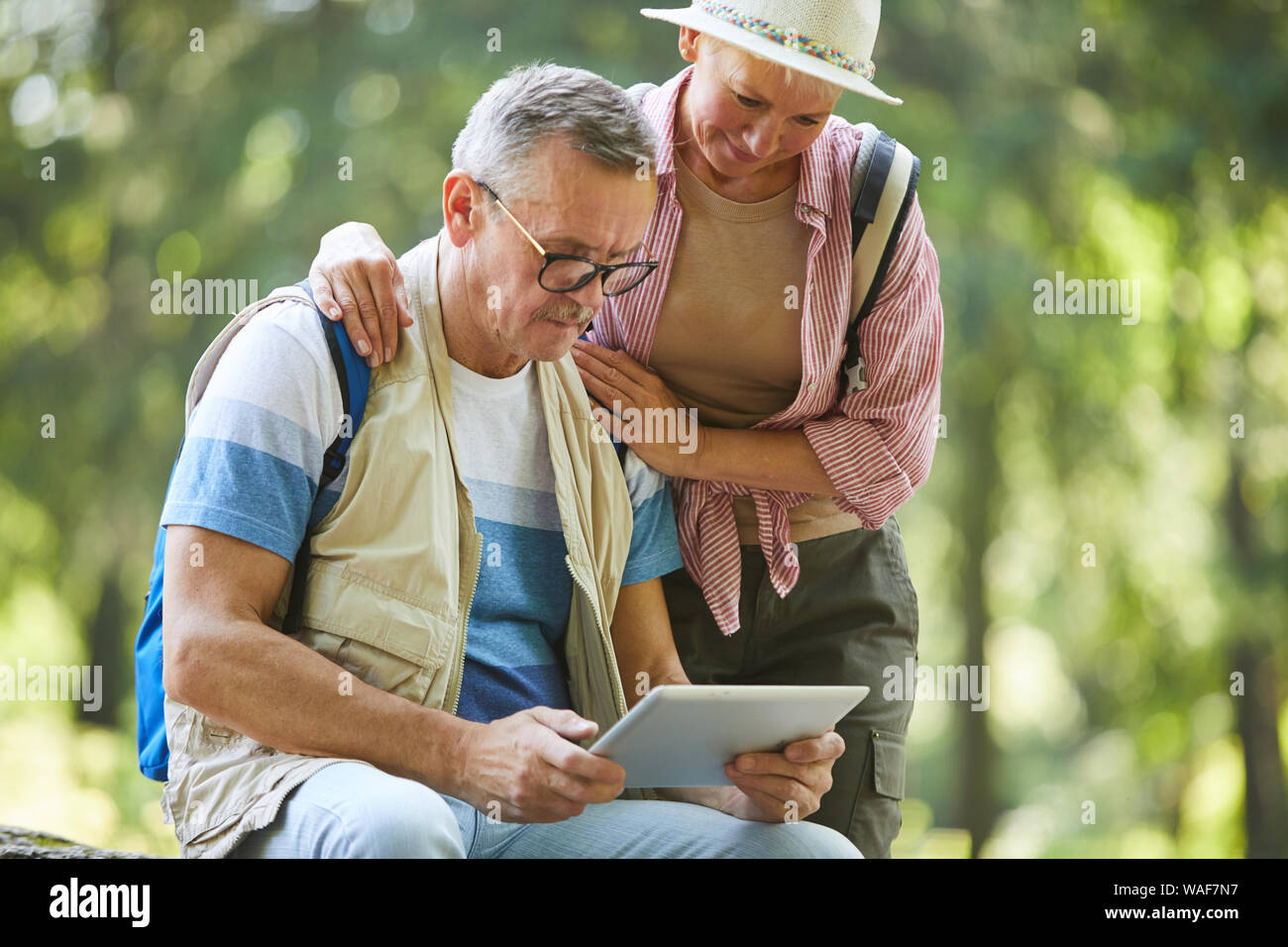 Ältere Menschen tragen Brillen sitzen und beobachten etwas auf digitale Tablette mit der älteren Frau, die in der Nähe von ihm, während Sie in den Wald sind Stockfoto