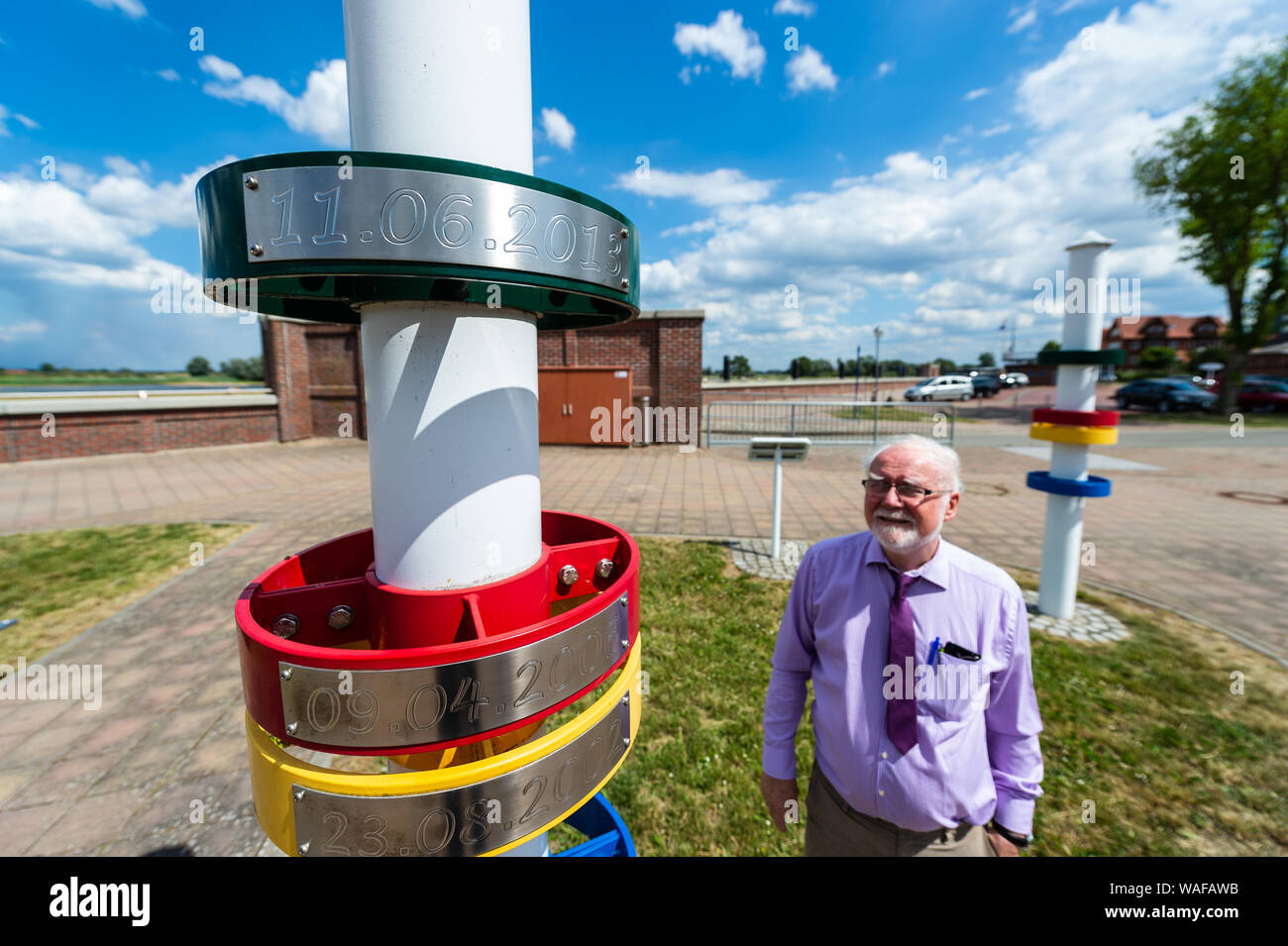 Hitzacker, Deutschland. 01. Juli, 2019. Peter Wieczorek, Hotelier und Vorsitzende des örtlichen Tourismus Verband, steht neben einer Spalte in der Nähe der Elbe in Hitzacker, wo die Wasserstände der Überschwemmungen von 2013 (grün), 2006 (rot), 2002 (gelb) und 2003 (blau) gesehen werden kann. Die Altstadt von Hitzacker liegt an der Elbe, eingerahmt von zwei Armen der kleinen Jeetzel. Aber die scheinbar idyllische Lage hat nicht nur wiederholt gefährdet die Gegend als die Stadt Insel bekannt. Die Altstadt wurde durch Überschwemmungen mehrmals getroffen, das letzte Mal es überschwemmt wurde im Jahr 2006. Credit: Philipp Schulze/dpa/Alamy leben Nachrichten Stockfoto