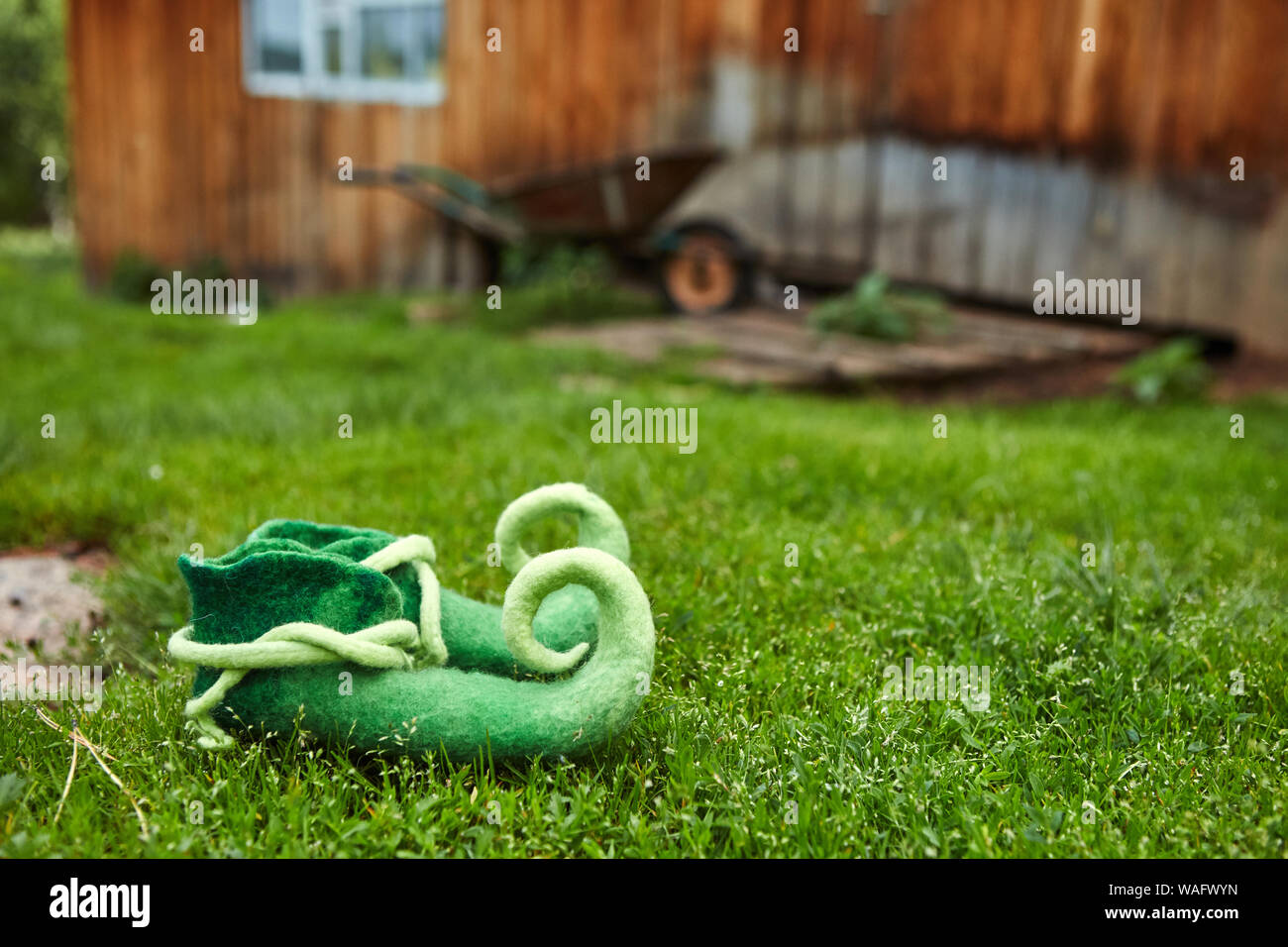 Schuhe Fabelwesen Stehend auf dem Gras, auf dem Hintergrund einer Holzhütte und einem kleinen dreirädrigen Warenkorb Stockfoto