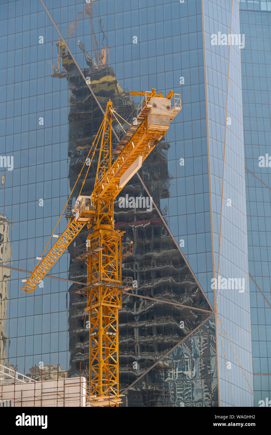 Vertikale Ansicht von einem gelben Kran mit Überlegungen zu einem Gebäude aus Glas. Stockfoto