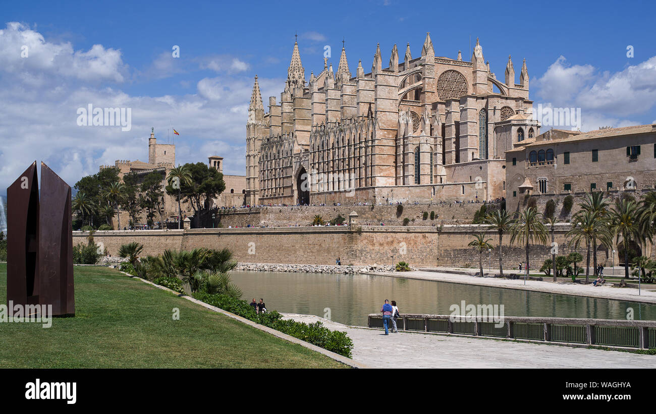 Majestätische Kathedrale von Palma de Mallorca über einen Kanal von Meer Wasser gesehen. Sonne Sommer leuchtet, Palmen und spanische Flagge dekoriert Stockfoto