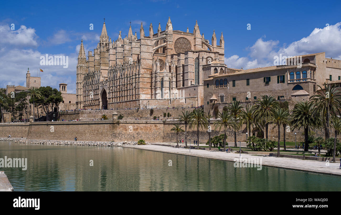 Majestätische Kathedrale von Palma de Mallorca über einen Kanal von Meer Wasser gesehen. Sonne Sommer leuchtet, Palmen und spanische Flagge dekoriert Stockfoto