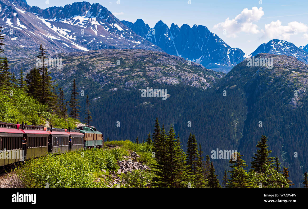 Eine schmale guage Tour Zug umarmt die Klippe an der White Pass Schlucht durch die Berge in der Nähe von Skagway Alaska Stockfoto