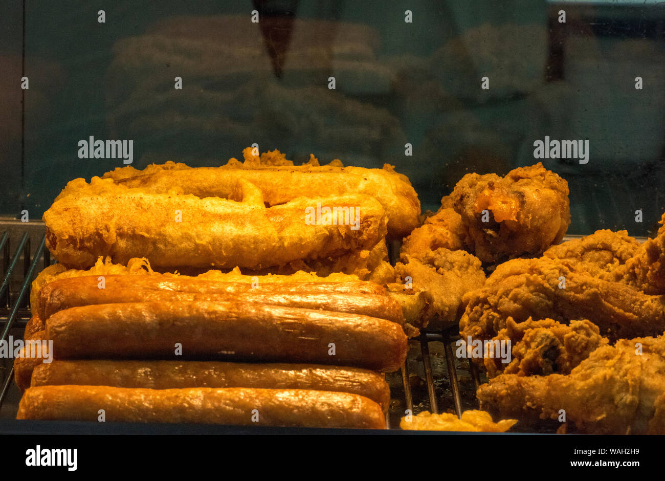 Fettsäuren frittierte Speisen und misshandelte Lebensmittel und Würstchen in einer heißen beheizten Zähler in einem Takeaway Fisch und Chip Shop. Stockfoto